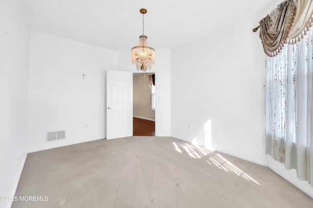 carpeted spare room with a wealth of natural light, visible vents, and an inviting chandelier