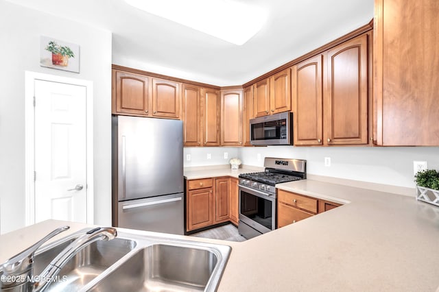 kitchen featuring brown cabinetry, stainless steel appliances, a sink, and light countertops