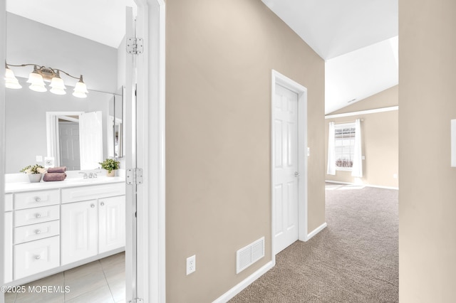 hallway with light tile patterned floors, light carpet, visible vents, baseboards, and vaulted ceiling