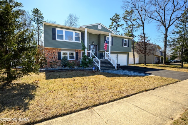 split foyer home featuring brick siding, driveway, a front yard, and a garage