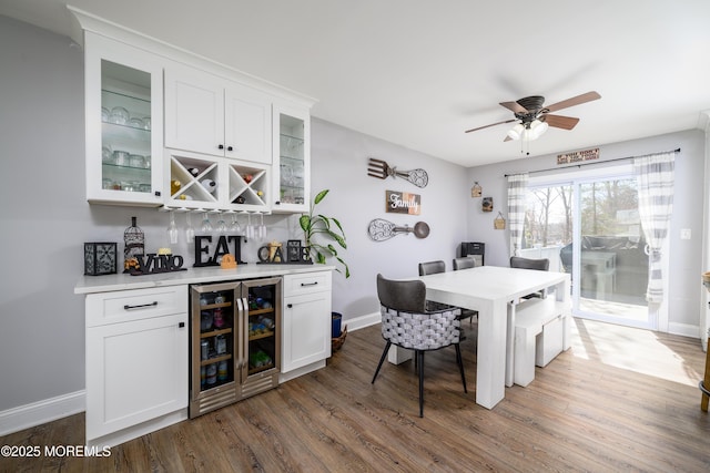 dining area featuring dark wood-style floors, baseboards, a bar, and beverage cooler