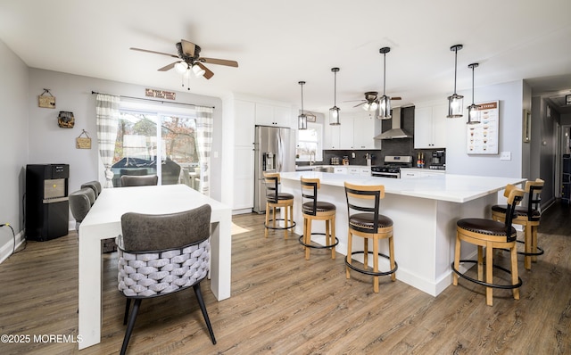 kitchen with ceiling fan, white cabinets, light wood-style floors, appliances with stainless steel finishes, and wall chimney range hood