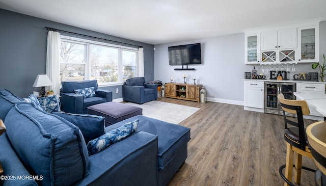 living area with a bar, wood finished floors, beverage cooler, and baseboards