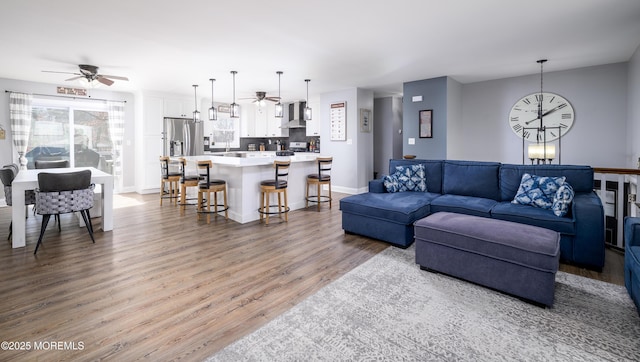 living room featuring ceiling fan with notable chandelier, wood finished floors, and baseboards