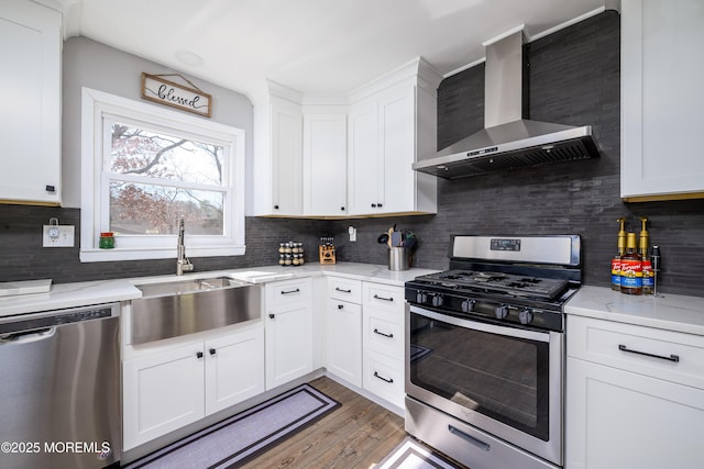 kitchen with a sink, stainless steel appliances, white cabinets, and wall chimney range hood