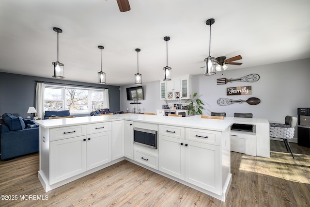 kitchen featuring stainless steel microwave, white cabinetry, light wood-type flooring, and open floor plan