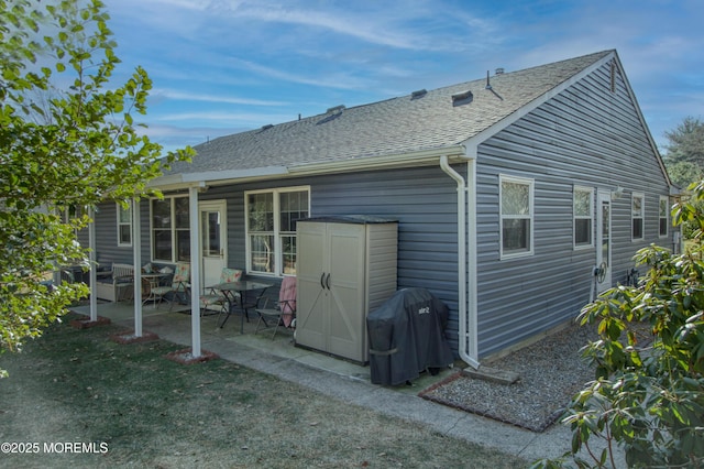 back of house with a storage unit, a shingled roof, a patio area, and an outbuilding