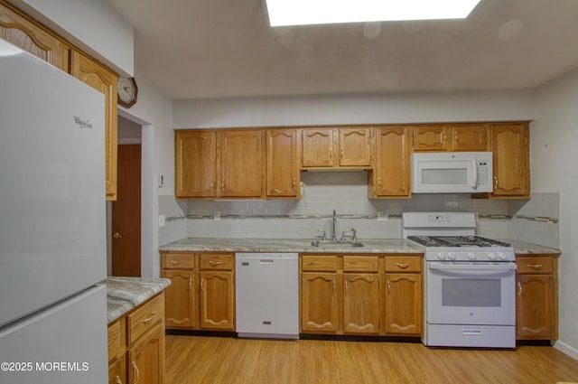 kitchen with white appliances, light wood-style floors, a sink, and brown cabinetry