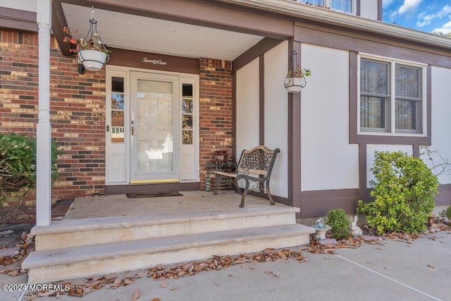 entrance to property featuring a porch and brick siding