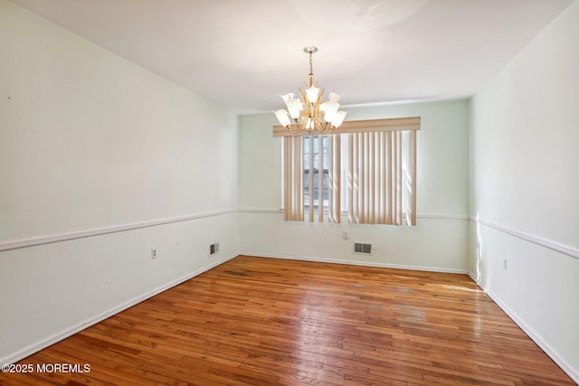 unfurnished room featuring an inviting chandelier, visible vents, and wood-type flooring