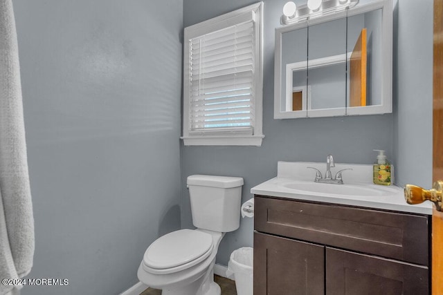 half bath featuring baseboards, toilet, and vanity