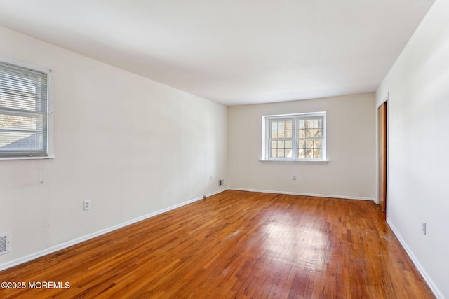 unfurnished room featuring visible vents, baseboards, and hardwood / wood-style floors