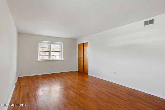 empty room featuring visible vents, baseboards, and hardwood / wood-style flooring