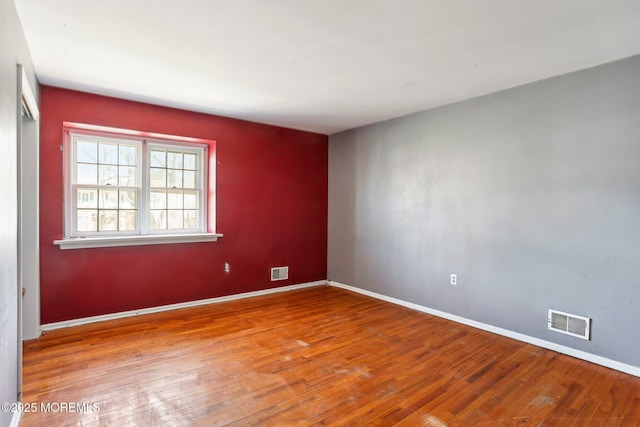 empty room featuring visible vents, baseboards, and hardwood / wood-style floors