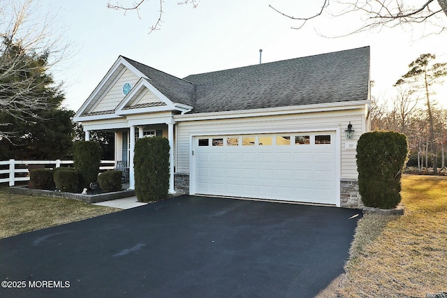 view of front of property with aphalt driveway, an attached garage, a shingled roof, fence, and stone siding