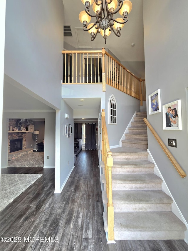 stairs featuring wood finished floors, baseboards, visible vents, a fireplace, and a towering ceiling