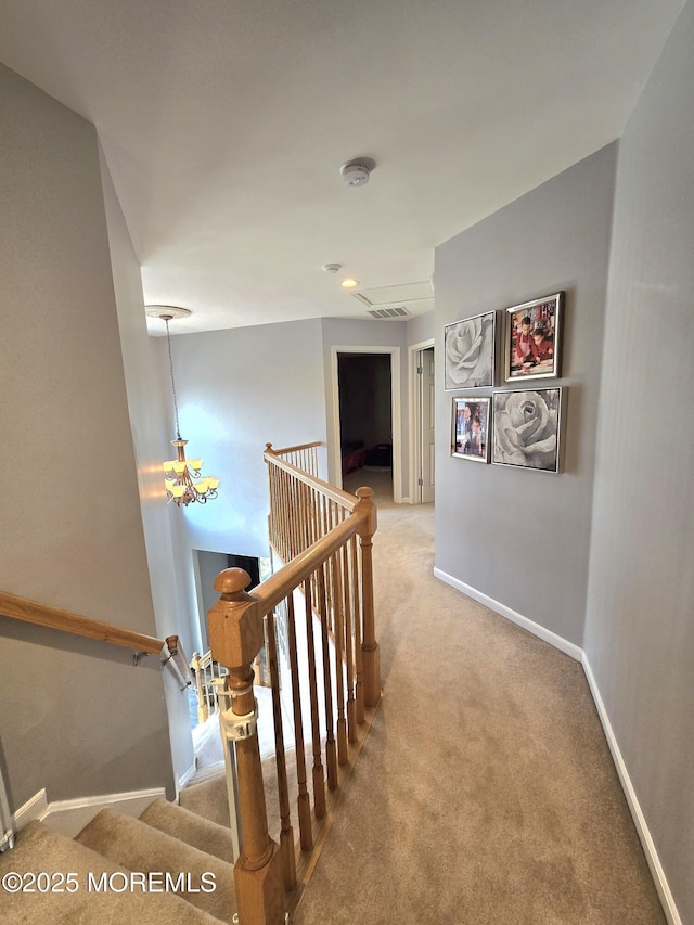 hallway with visible vents, baseboards, an upstairs landing, carpet flooring, and a notable chandelier