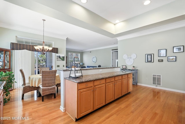 kitchen with visible vents, light wood-style flooring, dark stone countertops, crown molding, and a chandelier