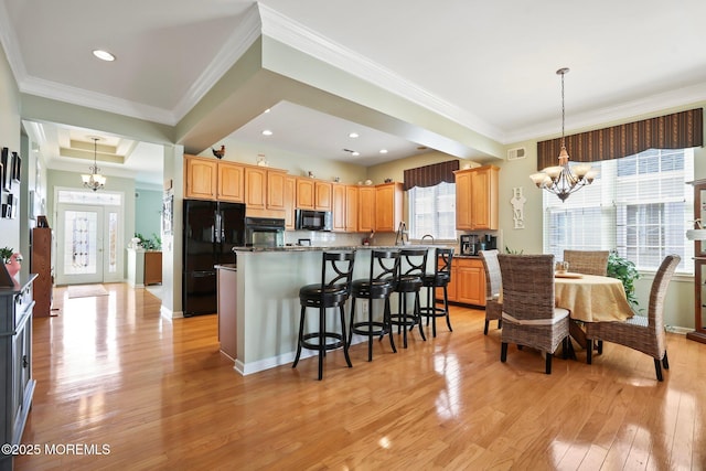 kitchen featuring light wood finished floors, a kitchen island, an inviting chandelier, black appliances, and a kitchen bar