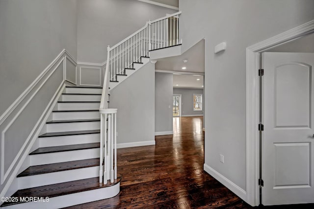 staircase featuring recessed lighting, a high ceiling, baseboards, and wood finished floors