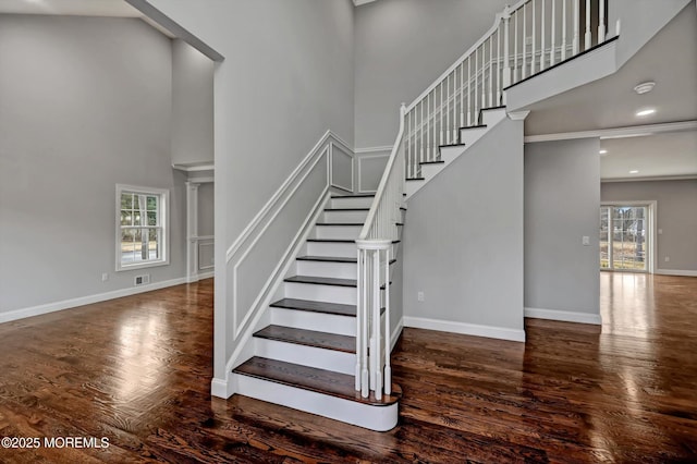 stairs featuring visible vents, baseboards, a high ceiling, and wood finished floors