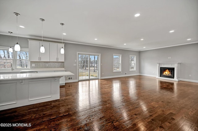 unfurnished living room featuring ornamental molding, a glass covered fireplace, recessed lighting, baseboards, and dark wood-style flooring