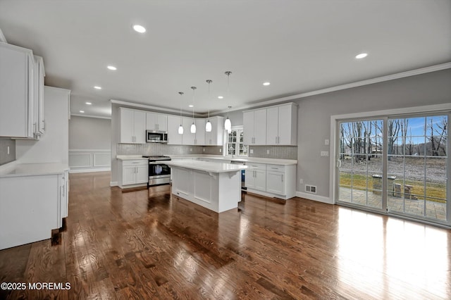 kitchen featuring a kitchen island, appliances with stainless steel finishes, ornamental molding, and dark wood finished floors