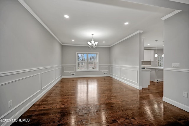 spare room featuring a notable chandelier, dark wood finished floors, ornamental molding, and a decorative wall