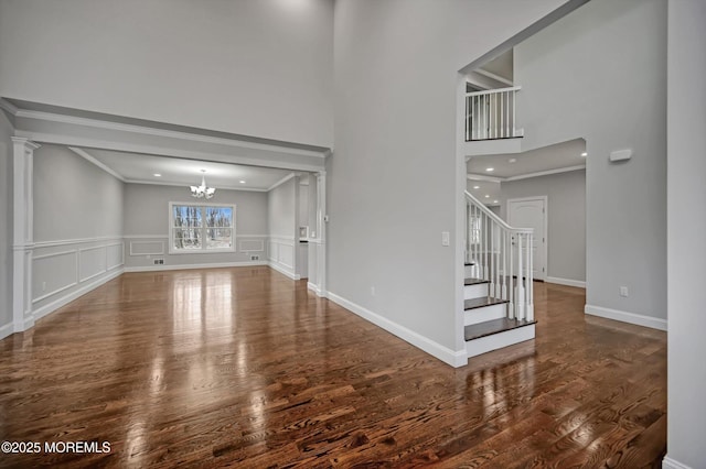 unfurnished living room with stairway, wood finished floors, crown molding, a decorative wall, and a chandelier