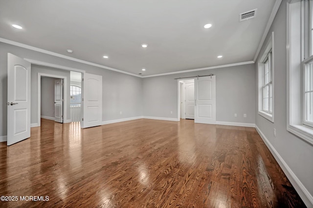 empty room with visible vents, wood finished floors, a barn door, crown molding, and baseboards