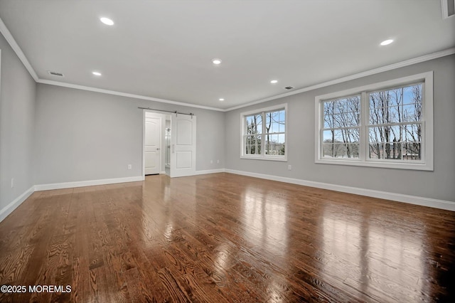 interior space with visible vents, baseboards, a barn door, ornamental molding, and wood finished floors