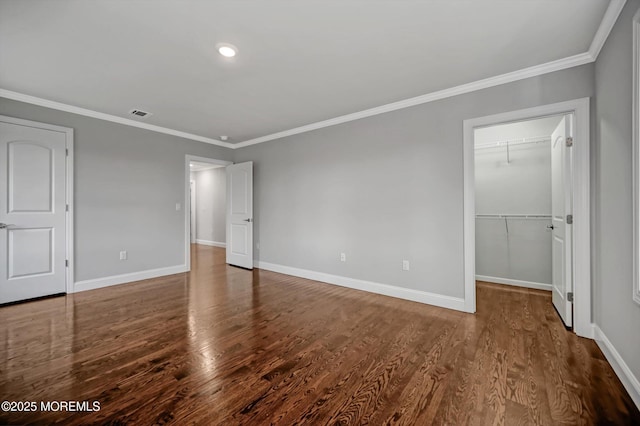 unfurnished bedroom with crown molding, a walk in closet, baseboards, and wood finished floors