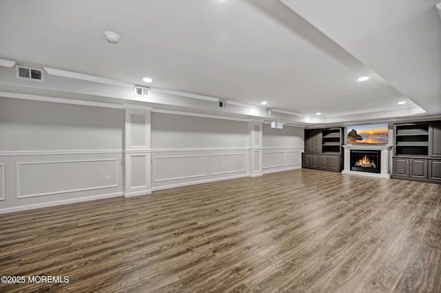 unfurnished living room featuring visible vents, a warm lit fireplace, wood finished floors, recessed lighting, and a raised ceiling