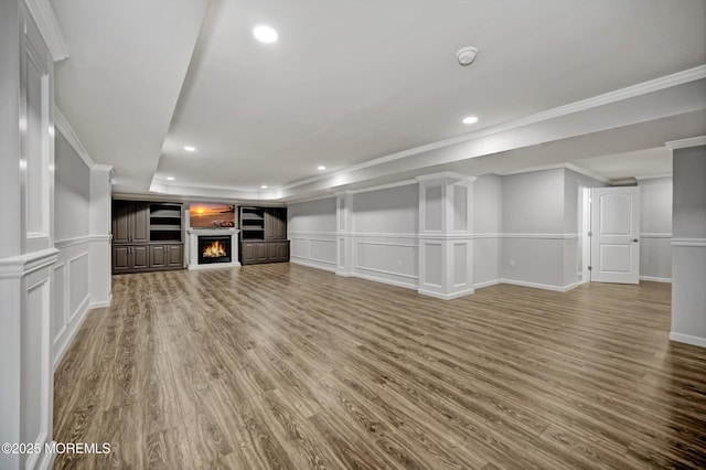 unfurnished living room featuring crown molding, a decorative wall, wood finished floors, and a warm lit fireplace