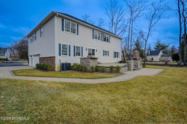 view of home's exterior featuring concrete driveway, central air condition unit, an attached garage, and a yard