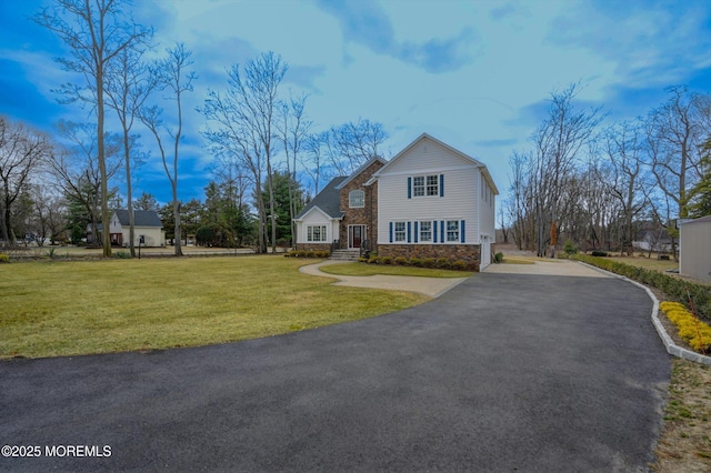 traditional-style house featuring a front yard, stone siding, and driveway