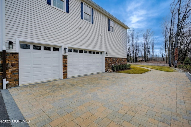 view of home's exterior featuring stone siding, driveway, and a garage