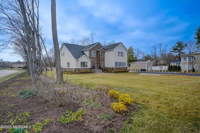 traditional-style house featuring stone siding, a front yard, an outdoor structure, and driveway