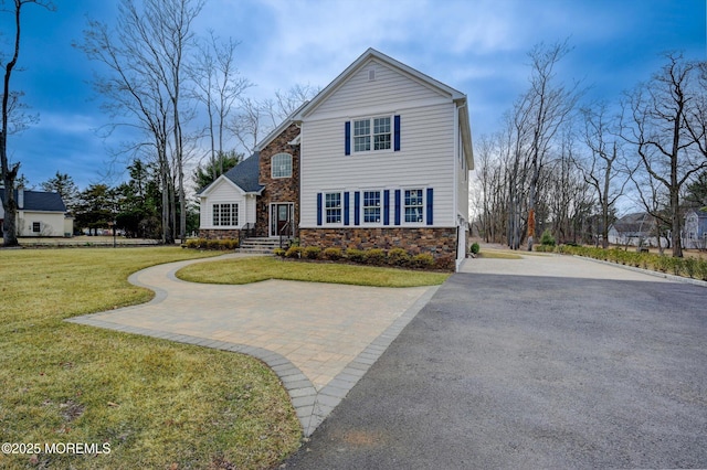 traditional-style house featuring a front lawn, stone siding, and driveway