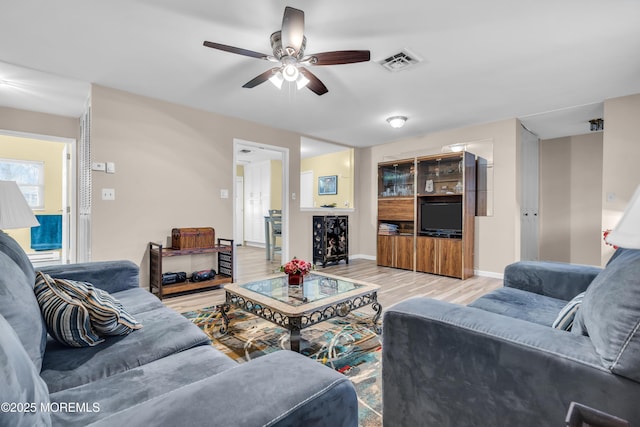 living room with light wood-style flooring, a ceiling fan, visible vents, and baseboards