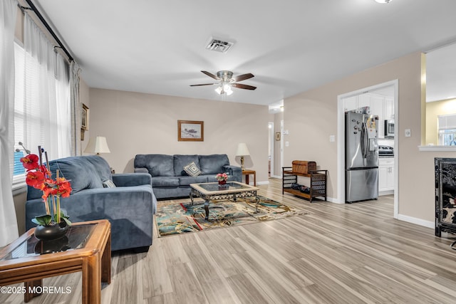 living area featuring baseboards, visible vents, ceiling fan, and light wood finished floors