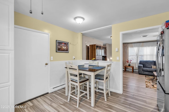 dining area featuring light wood-style floors, wainscoting, and tile walls