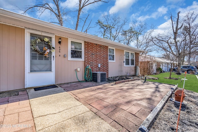 exterior space with a patio area, a lawn, brick siding, and central AC unit