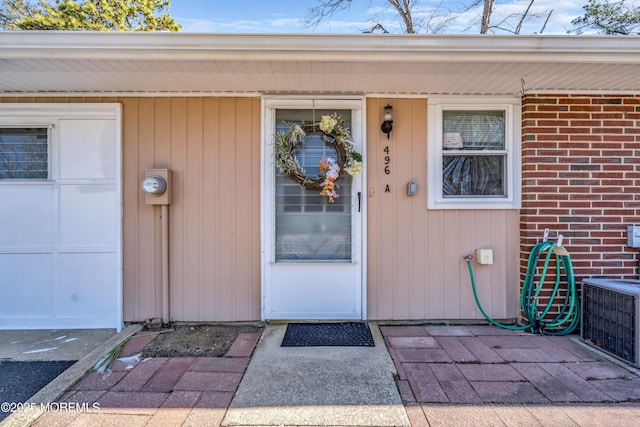 doorway to property featuring a garage, brick siding, and cooling unit