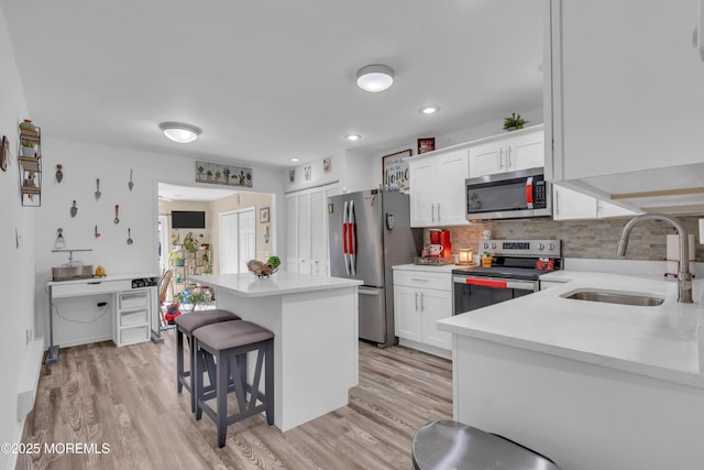 kitchen with a kitchen island, a kitchen bar, stainless steel appliances, white cabinetry, and a sink