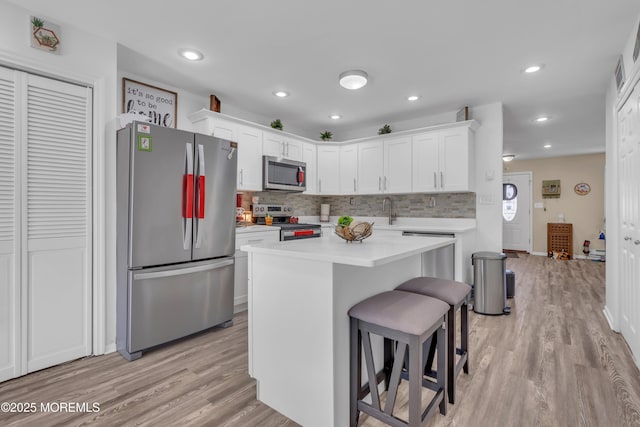 kitchen featuring light wood-type flooring, stainless steel appliances, white cabinets, light countertops, and decorative backsplash