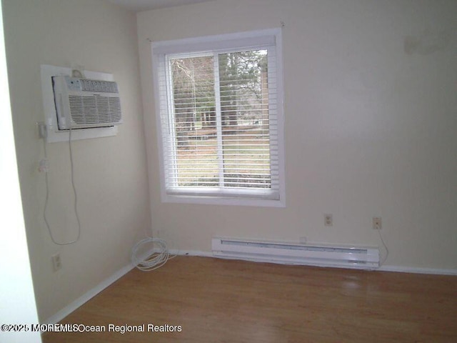 empty room featuring a wall unit AC, baseboards, a baseboard heating unit, and wood finished floors