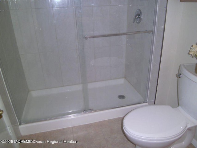 bathroom with a stall shower, toilet, and tile patterned floors