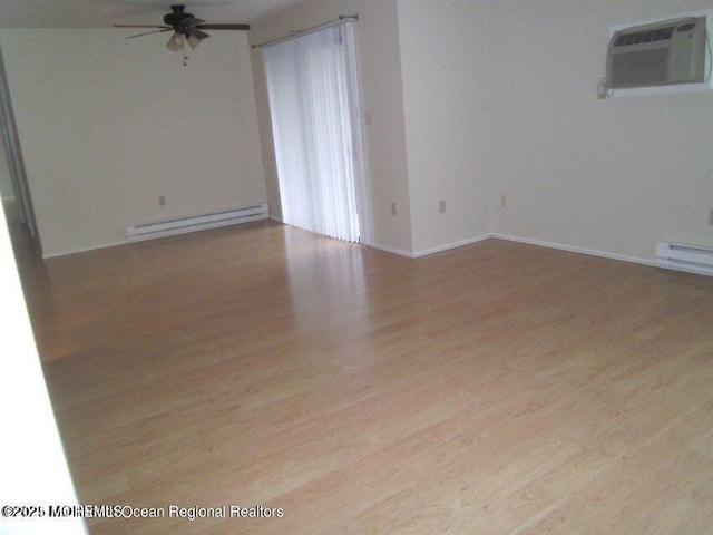 spare room featuring a wall unit AC, baseboard heating, a ceiling fan, wood finished floors, and baseboards