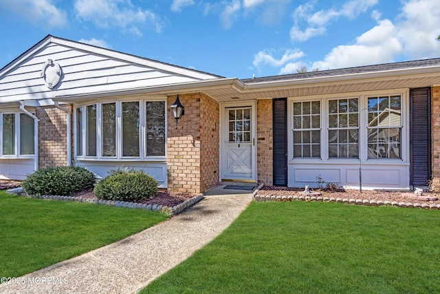 view of exterior entry with a yard and brick siding